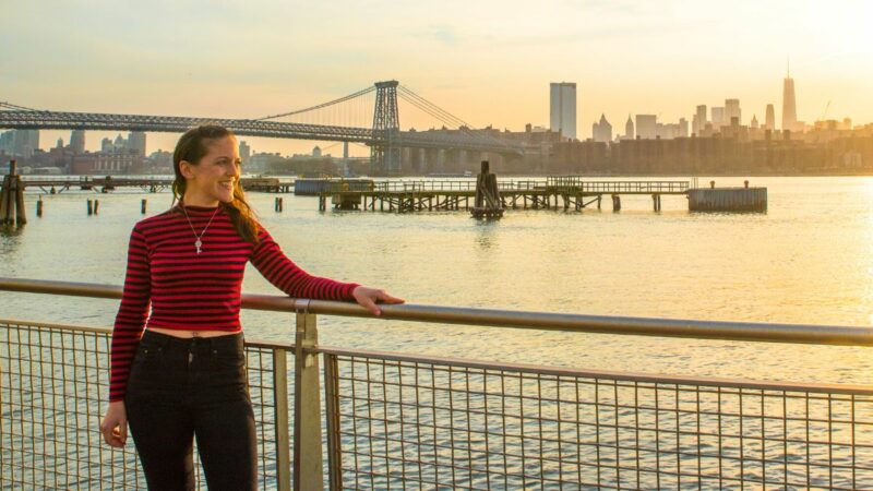 在布鲁克林徒步旅行时，一位女士站在东河前，背景是纽约的天际线