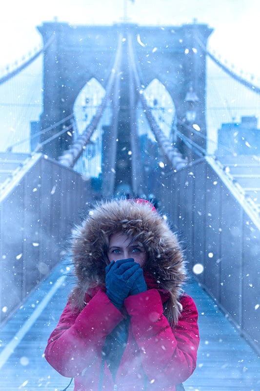 一名身穿红色外套的女子在纽约布鲁克林大桥上摆姿势拍冬季照