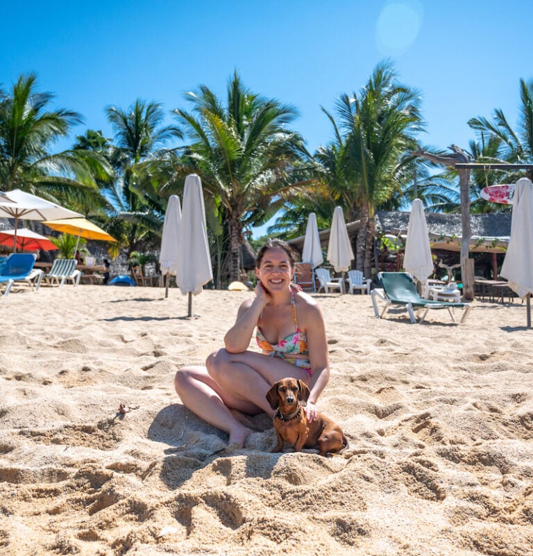 在巴亚尔塔港的海滩上，独自一人的女性旅行者带着一只狗
